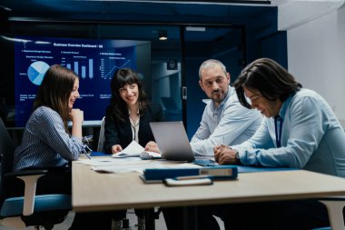 Üst düzey bir şirket yönetim kurulundaki yatırım riskini değerlendiren beyin fırtınası oturumunda aralarında yönetici ve asistanların da yer aldığı dört profesyonel işbirliği yapıyor. Stratejik toplantı, lüks ofis ortamında takım çalışması ve analizleri gösteriyor..