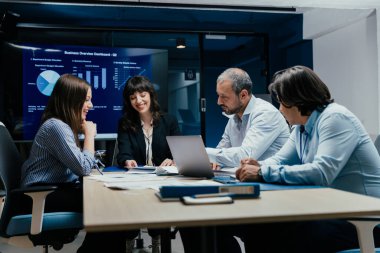 Üst düzey bir şirket yönetim kurulundaki yatırım riskini değerlendiren beyin fırtınası oturumunda aralarında yönetici ve asistanların da yer aldığı dört profesyonel işbirliği yapıyor. Stratejik toplantı, lüks ofis ortamında takım çalışması ve analizleri gösteriyor..