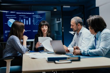 Üst düzey bir şirket yönetim kurulundaki yatırım riskini değerlendiren beyin fırtınası oturumunda aralarında yönetici ve asistanların da yer aldığı dört profesyonel işbirliği yapıyor. Stratejik toplantı, lüks ofis ortamında takım çalışması ve analizleri gösteriyor..