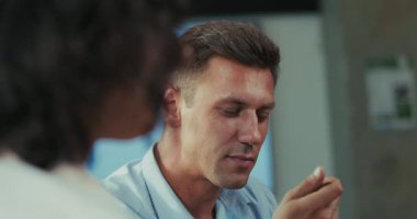 Kafkasyalı bir adamın sağlıklı salatasını yerken, bir iş arkadaşının parlak, rahat bir ofis kafeteryasında güzel yeşil ve doğal ışıklandırmalı konuşmasını dikkatle dinlediği yavaş çekim videosu..