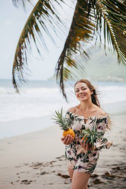 Ellerinde ananaslarla tropik sahilde güzel bir kız