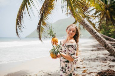 Ellerinde ananaslarla tropik sahilde güzel bir kız