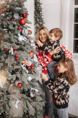 Genç ve güzel bir anne ve çocukları bir Noel ağacı süslüyorlar.
