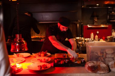 The chef in a black uniform decorates the food on the plates