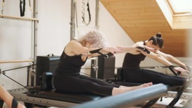 Rehabilitasyon ve sağlıklı yaşam tarzı, miyofasyal tahliye kavramı. Modern stüdyo kişisel antrenmanında üst üste pilates reformatöründe karın kası ameliyatı yapan bir grup kadın.