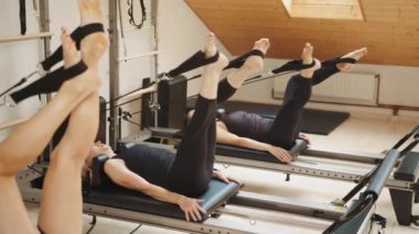 Bir kadın sağlık ve zindelik konseptinde bir spor salonundaki ıslah yatağında kayış kullanarak pilates köşegen dengeleme egzersizi yapıyor. Fitness konsepti.