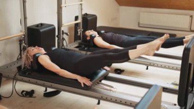 Rehabilitasyon ve sağlıklı yaşam tarzı, miyofasyal tahliye kavramı. Modern stüdyo kişisel antrenmanlarında üst üste pilates reformatörüyle karın kası yapan bir grup kadın. Fitness konsepti.