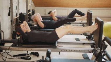 Fitness konsepti. Rehabilitasyon ve sağlıklı yaşam tarzı, miyofasyal tahliye kavramı. Modern stüdyo kişisel antrenmanında üst üste pilates reformatöründe karın kası ameliyatı yapan bir grup kadın.