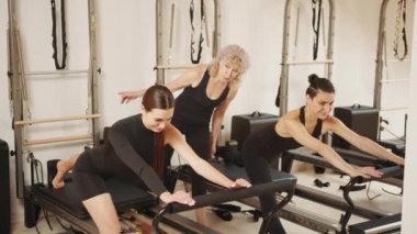 Kişisel antrenör, takım çalışması, egzersiz, formda. Pilates stüdyosunda spor eğitmeni desteğiyle mekik çeken zinde bir kadın. Spor merkezinde kişisel antrenör, pilates stüdyosu iç mimarisi.