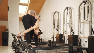 Rehabilitasyon, sağlıklı yaşam tarzı, küçük işletme konsepti. Profesyonel yetişkin kadın fitness koçu kızlara pilates reformatında doğru egzersizi yapmayı öğretiyor. Fitness konsepti