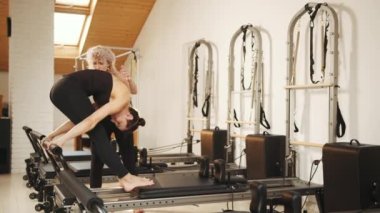 Fitness konsepti. Rehabilitasyon, sağlıklı yaşam tarzı, küçük işletme konsepti. Profesyonel yetişkin kadın fitness koçu kızlara pilates reformatında doğru egzersizi yapmayı öğretiyor.