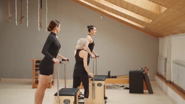 Pilates Lesson Chair Side View Blond Elderly Personal Trainer Coaching — Vídeo de Stock