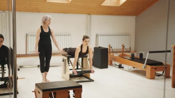 Pilates Lesson Chair Side View Blond Elderly Personal Trainer Coaching — Vídeo de Stock