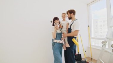 A cheerful happy family is renovating a purchased apartment. A very smiling family of three people taking a selfie. The child hugs his parents tightly. In the background, repairs are taking place