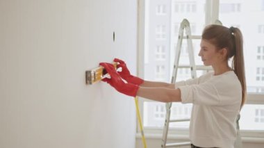 Young woman using leveling tool at home. A happy family is renovating a purchased apartment. Repair, building and home concept - smiling couple building new home using spirit level to measure.
