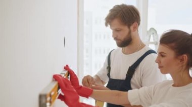 Repair, building and home concept - smiling couple building new home using spirit level to measure. Young woman using leveling tool at home. A happy family is renovating a purchased apartment
