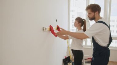 Smiling couple doing repair at home using spirit level to measure. Repair, building and home concept. Young woman using leveling tool at home. A happy family is renovating a purchased apartment