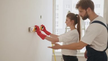 A happy family is renovating a purchased apartment. Smiling couple doing repair at home using spirit level to measure. Repair, building and home concept. Young woman using leveling tool at home