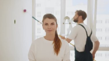 Roulette. Young fun beautiful woman in casual clothes holding measure tape. Instruments, accessories for renovation apartment room. Repair home concept. In the background, a man paints a wall.