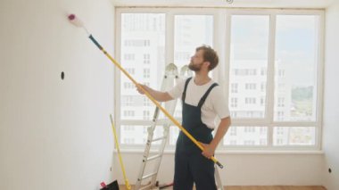 Happy couple painting walls in their new house. Cheerful couple young man and woman, painting white wall with roller during renovation in new apartment. Couple is repairing and painting the wall.