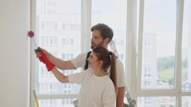 Couple Decorating Room In New Home Painting Wall Together. Happy couple renovating their new house and painting interior walls together: lifestyle, home makeover and remodeling concept