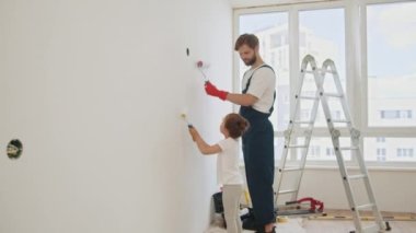 Happy father teaching little adorable kid girl daughter how to paint wall using paintbrush. Painting on background. Home renovation and repair concept. Painting a wall in new home