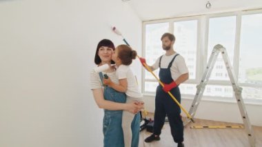 Happy family renovating their home. They are painting a wall together. Portrait of young family who does repair at home, father stands and paints the wall. Repair in the apartment