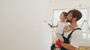 The child helps her father in the repair. Repair in the apartment. Happy family father and child daughter paints the wall with paint. Smiling 4-year-old girl holds a paint roller in her hands