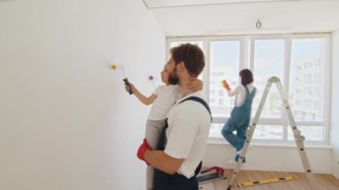 Happy family mother and child daughter making repairs, paint the wall at home. Family time together with their young daughters father shows his children how to paint a wall with a roller