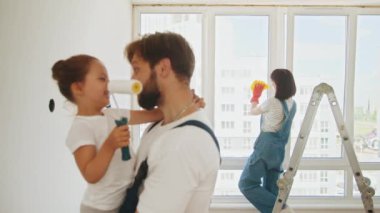 Joyful young Caucasian family painting room. Dad teaching little adorable daughter to paint wall using roller brush. Family time together with their young daughter father, paint a wall with a roller