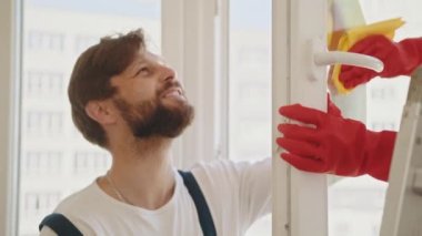 Tulumlu temizlik işçileri bir apartman dairesinde deterjan püskürtüyor ve pencere camlarını siliyorlar. Camları sprey şişeyle siliyorum. Bir grup işçi apartmanın camlarını temizliyor.