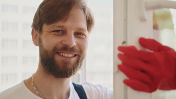 Zabawny Młody Facet Zadbaną Brodą Specjalnych Ciuchach Spryskujący Okno Detergentem — Wideo stockowe
