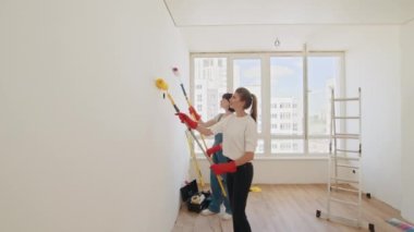 Yeni evlerinin duvarlarını boyamak için boya silindiri kullanan iki bayan arkadaş. Duvarı boya rulosuyla boyayan iki genç kadın. Odada tamirat yapan mutlu kadınlar. Kadın elleri onarılıyor