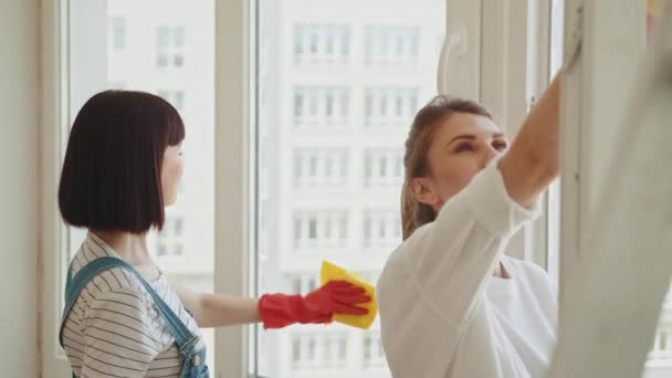 清洁服务 女人很快乐两个积极的女性清洁室在一起 女用手套清洁窗户 家里用清洁剂喷雾器和黄色标签 — 图库视频影像