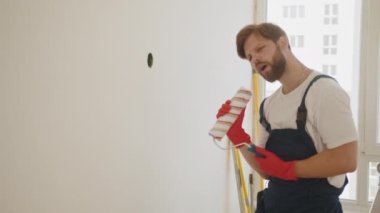 Paten fırçasını mikrofon olarak kullanan mutlu beyaz erkek şarkı söylüyor. Genç adam tadilat ve tadilat sırasında eğleniyor. Odada duvar boyayan genç bir işçi. Mutlu beyaz erkek şarkı söylüyor