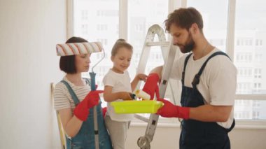 Mutlu aile, anne, baba ve çocuk evde boya duvarlarını onarıyor. Genç Baba ve Anne, Çocuklarına Bir Duvar Nasıl Boyanır Gösteriyorlar. Dairede tamirat var..