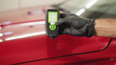 Closeup view of male hand, using film coating thickness gauge device to check car paint. Auto coating quality control. Inspector measuring paint cover thickness at the vehicle detailing service.