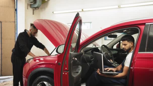 Молодой Механик Использующий Ноутбук Сидящий Внутри Красной Машины Коллега Планшетом — стоковое видео