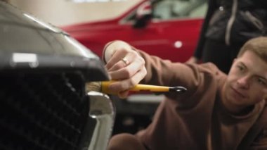 Car washing, detailing concept. Side view of caucasian man worker of car wash service cleaning headlights of luxury grey car using green spray bottle. Male worker cleaning car headlights.