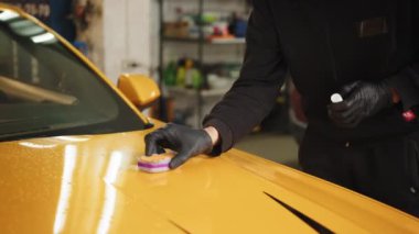Genç adam, araba cilası işçisi araba kaputunu cilalıyor, sarı renkli spor arabayı nano seramik kompozisyon ya da balmumuyla cilalıyor. Araba tamiri. Cilalama araçları.