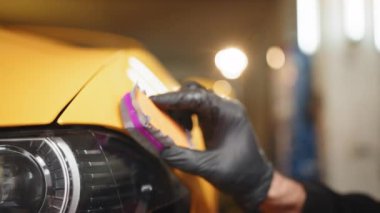Tsar service worker applying nano coating on a Tsar detail. Professional male auto service worker polishing and detailing a car body, waxing car hood and headlight with a wax or nano ceramic coating
