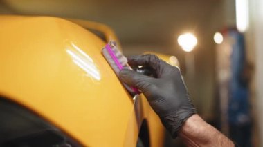 Tsar service worker applying nano coating on a Tsar detail. Professional male auto service worker polishing and detailing a car body, waxing car hood and headlight with a wax or nano ceramic coating