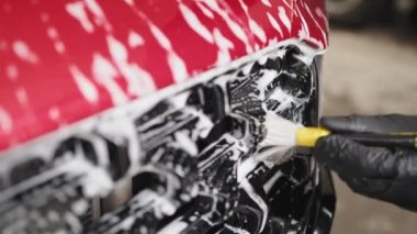 Closeup view of hand with special yellow brush of wash worker cleaning red crossover grille in a vehicle detailing workshop. Auto service industry. Car washing concept