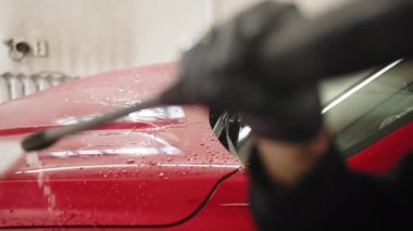 Cropped view of a man worker cleaning modern red automobile with high pressure water at car wash. Car wash service and detailing concept. Car wash service and detailing concept.