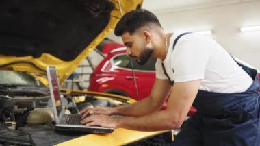 Ciddi odaklı erkek araba teknisyeni motor tamir sorunu, sistem kontrolü sırasında, araba garajında bakım ve onarım için tablet bilgisayar kullanılıyor.