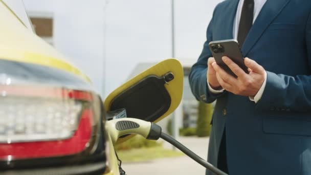 Mężczyzna Odłączanie Kabla Zasilającego Samochodu Elektrycznego Pomocą Aplikacji Smartfonie Biznesmen — Wideo stockowe