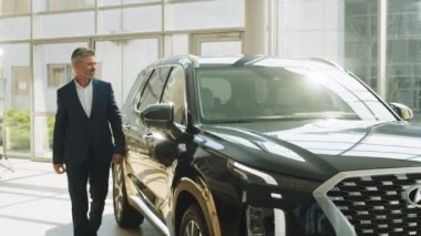 LVIV, UKRAINE - 20 Temmuz 2022: Showroom ve araba galerisi Hyundai. Yandan bakıldığında mutlu iş adamı erkek müşteri 45 'likler mavi takım elbise giyer ofise girer ve araba galerisine bakar..