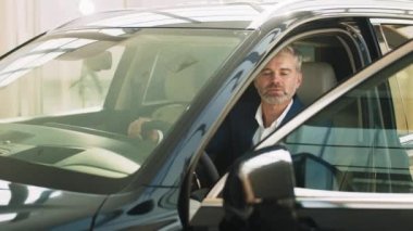 Gri sakallı, yakışıklı, olgun bir adamın portresi. Gıcır gıcır bir arabada oturuyor. Güneşli bir günde motorlu taşıt kullanan yetişkin bir adam, pencereden bir portre ile yakalandı..