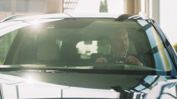 一个英俊的男人从经销商那里买到新车后很高兴 现代经销商商店 成功的商人穿着正装坐在驾驶座上 试驾汽车 — 图库视频影像
