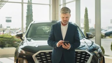 Orta yaşlı, olgun, yakışıklı, sakallı, takım elbiseli, beyaz saçlı bir adamın portresi. Arabasına yaslanmış ve almalı mı diye düşünüyor. Otomobil galerisinde yeni arabanın yanında duran müşteri